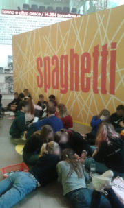 Ragazzi che lavorano allo slogan seduti sotto un cartellone con scritto spaghetti