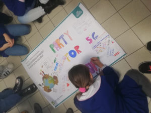 Bambina scrive la propria idea sul cartellone Vuoi cambiare il mondo? lascia qui la tua idea